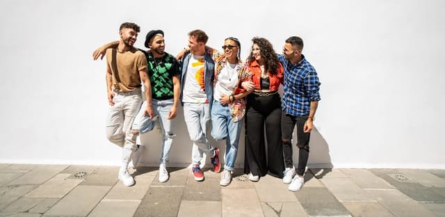 Group of happy young friends having fun and laughing, standing over white wall. Diverse millennial people spending time together. Friendship concept. Real people lifestyle.
