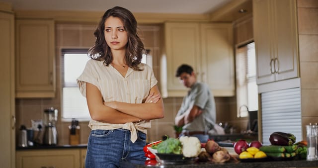 Shot of a young woman looking upset after a fight with her boyfriend who is standing in the background