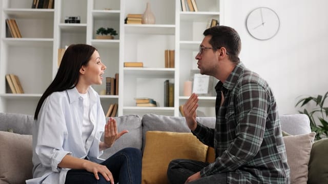 A young couple is sitting on the sofa in the living room, emotionally arguing about important things, discussing problems in the relationship, they cannot come to an agreement