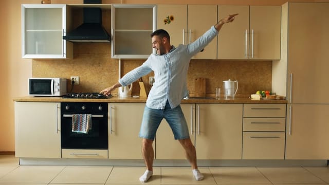 Handsome young funny man dancing in kitchen at home in the morning and have fun on vacation