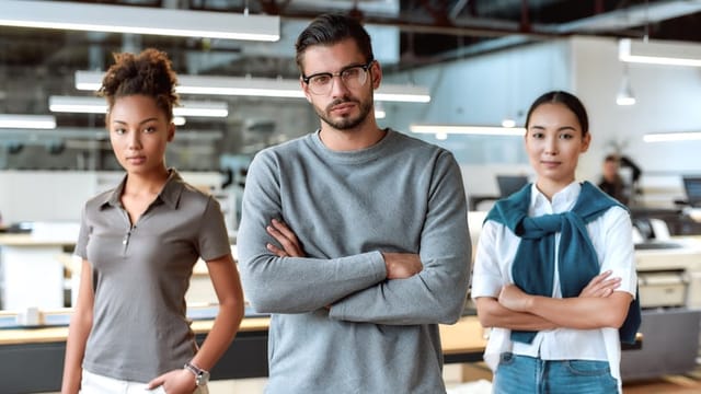 Portrait of three ambitious co-workers in casual wear. Two women and man looking at camera, while standing in working space. Teamwork concept. Horizontal shot. Front view. Selective focus
