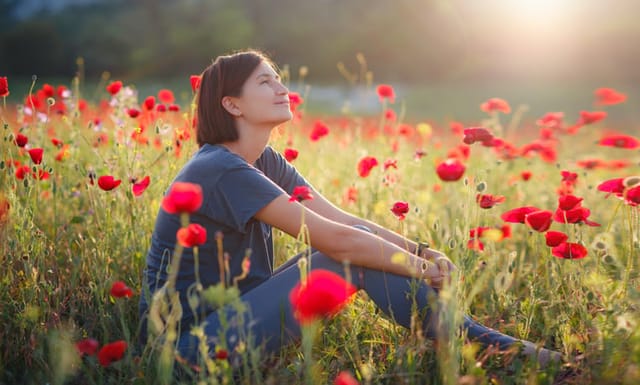 A beautiful woman meditates on a poppy field at sunset. Wellness well-being happiness concept.