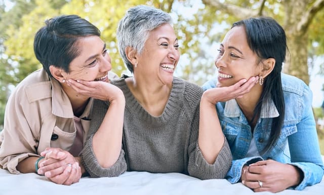 Family, love and lesbian couple with adult daughter, happy and laughing, relax and talking in a park. Lgbt, happy family and woman enjoying a picnic with her mothers, cheerful and excited while lying