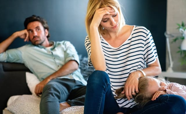 Tired mother and father sitting on couch feels annoyed exhausted stressful with little girl child.