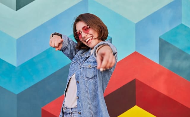 Happy hipster female in denim clothes and sunglasses pointing 