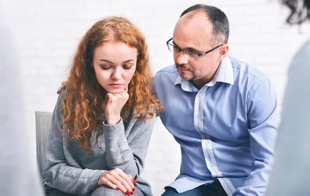 Caring husband supporting his depressed wife at marriage therapy session in counselor's office, encouraging her to share problems