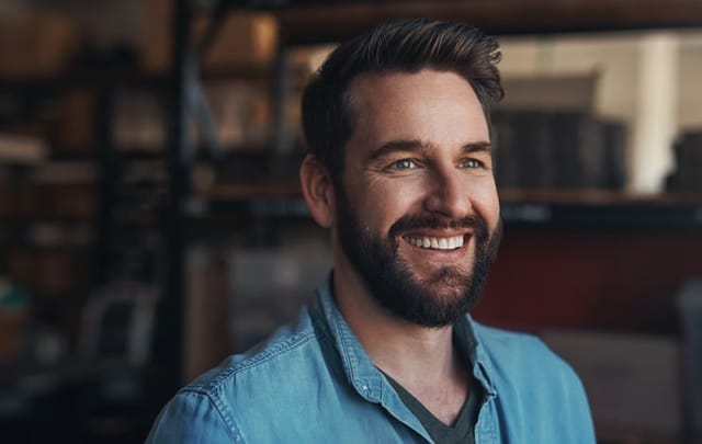 Happy, smile and young man in a studio with positive, good and confident attitude for small business. Happiness, pride and male person from Canada with entrepreneurship mindset in a modern office.