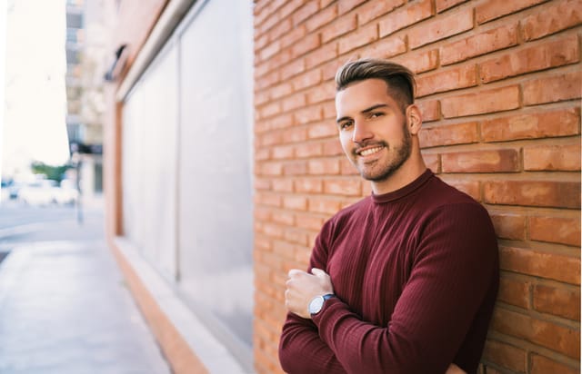 smiling man crossed arms outdoors brick wall