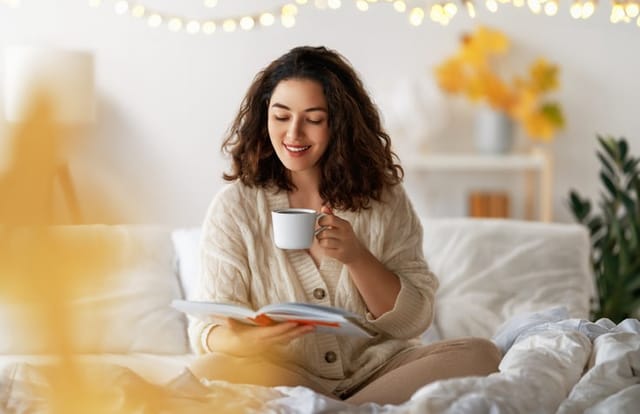 Portrait of young woman enjoying a cup of coffee at home. Smiling pretty girl drinking warm beverages. Good time at home.