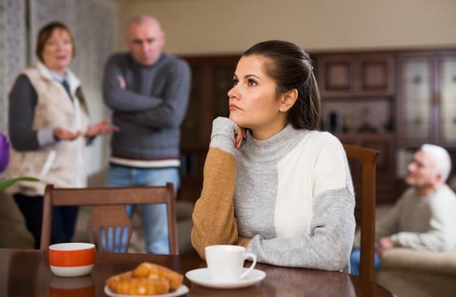 Portrait of upset woman sitting at home table after quarrel with husband and his parents