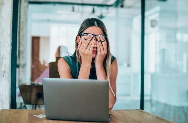 woman covering eyes at computer desk