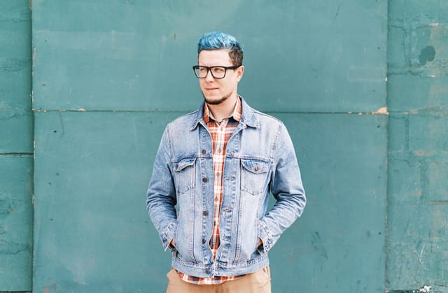 blue-haired man standing against blue wall