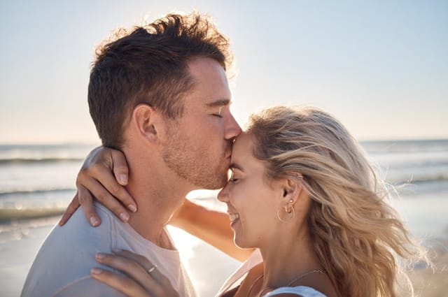 man kissing girlfriend's head at beach