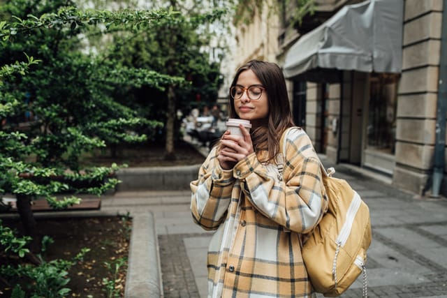 girl with eyes closed and coffee on street