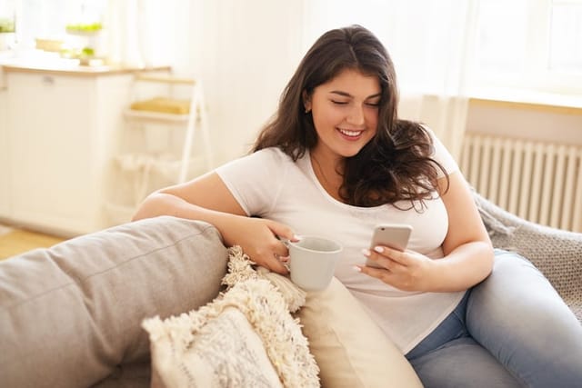 woman texting on couch with tea