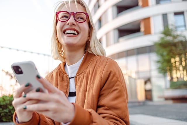 smiling blonde woman texting outside