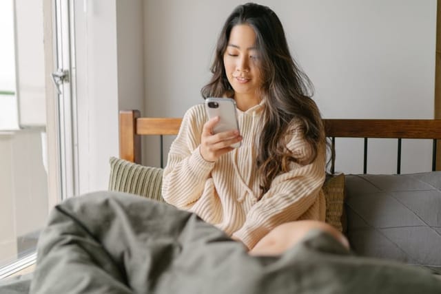 asian woman reading texts in bed smiling
