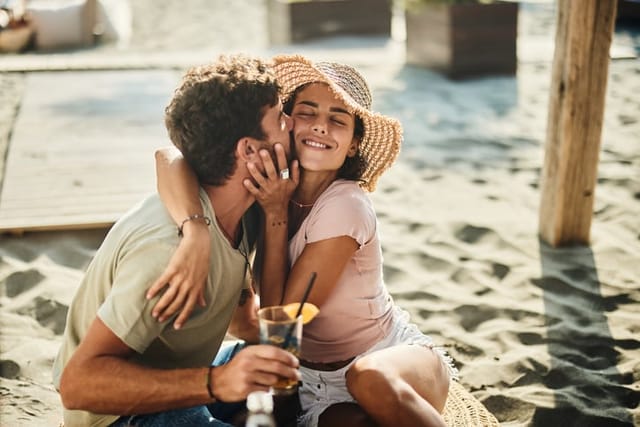 man kissing woman's cheek on beach