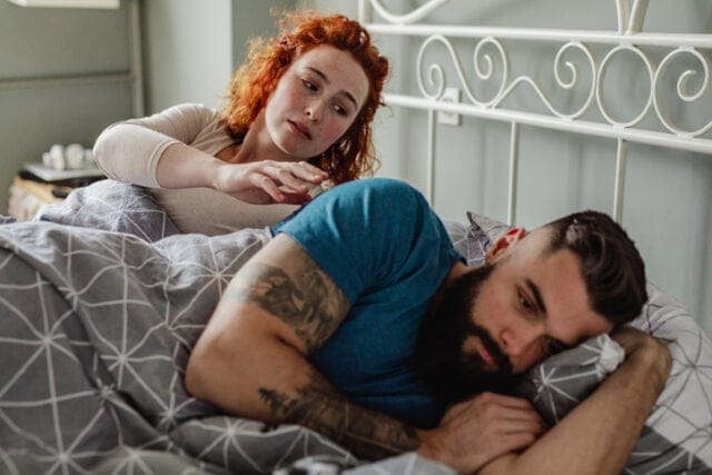 woman reaching for upset boyfriend in bed