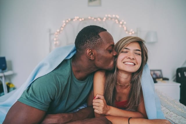 man kissing woman's cheek in bed