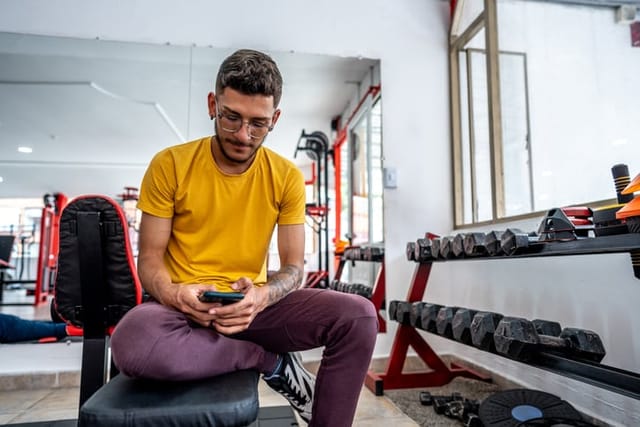guy texting in gym on weight bench