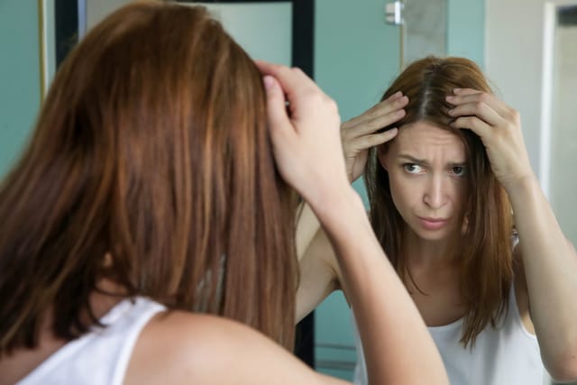 woman examining scalp in mirror