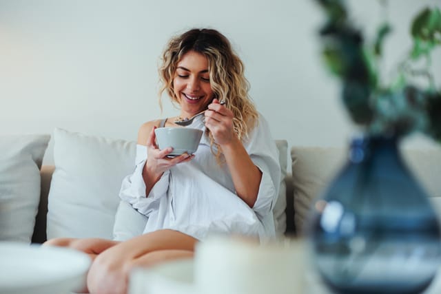smiling woman eating yogurt on couch