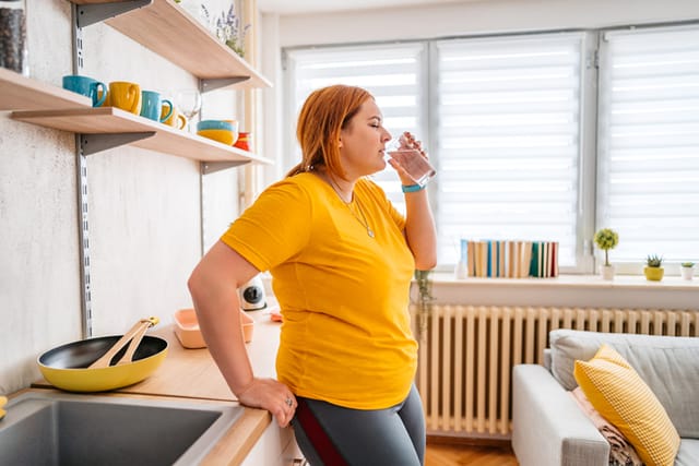 redhead woman drinking water in kitchen
