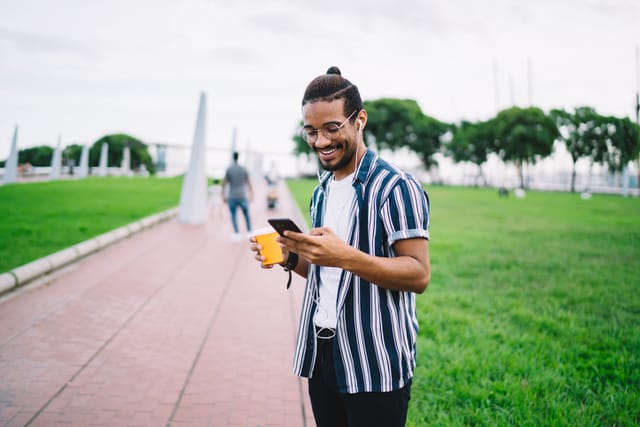 smiling hipster guy texting in park