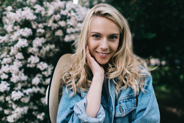 smiling blonde woman with hat in front of flowers