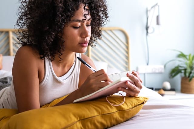 woman writing in journal in bed