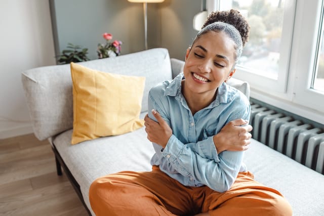 smiling woman hugging herself on couch