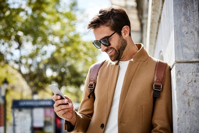 smiling trendy guy texting in sunglasses