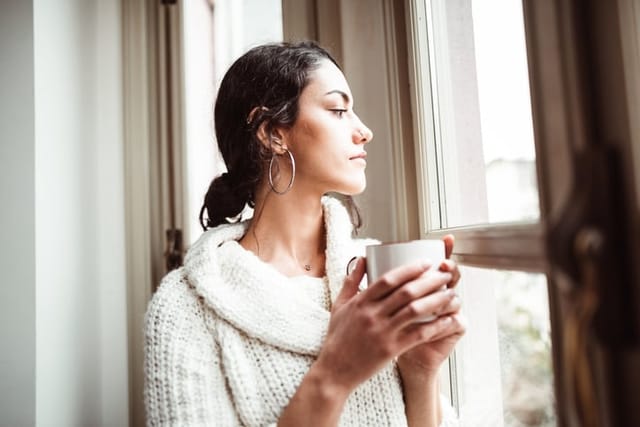 serious woman looking out window with mug