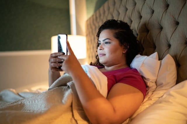 smiling woman texting sitting in bed