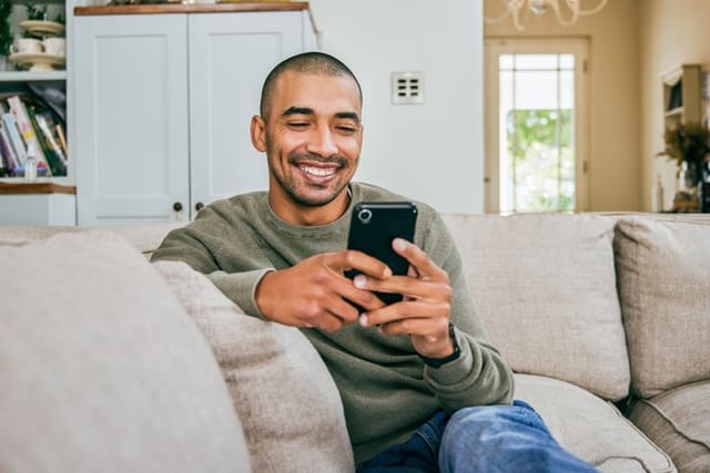 smiling man texting on couch