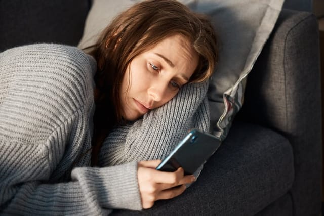 depressed woman texting laying down on couch