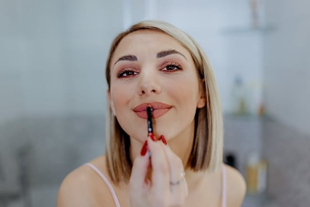 woman applying lipstick in bathroom mirror