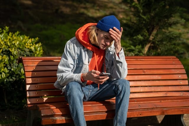 sad guy texting on park bench