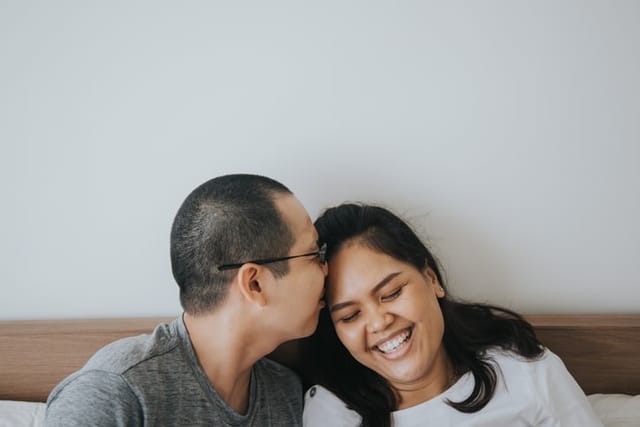 man kissing smiling girlfriend's forehead