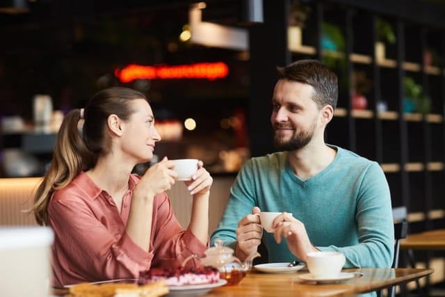 Young couple sitting at the table with cup of tea and talking to each other during their date in cafe