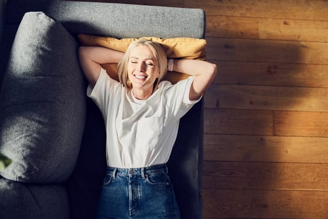 Laughing adult woman lying on the sofa at home relaxing with eyes closed