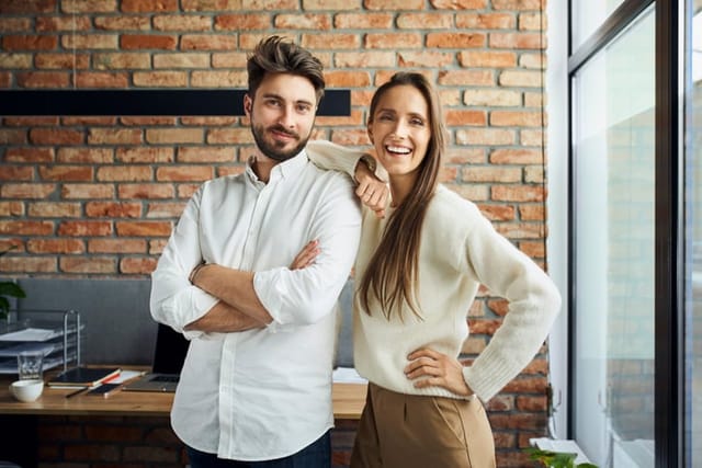 Portrait of successful couple standing at small office. Happy new business partners posing together