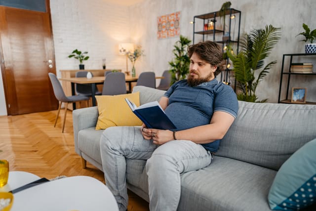 Overweight young man relaxing at home and reading a book.