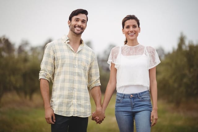 Smiling young couple holding hands while looking away at olive farm