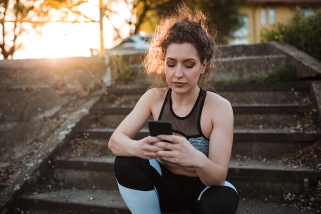 Young woman in sportswear is using her mobile phone while sitting on stairs outdoors