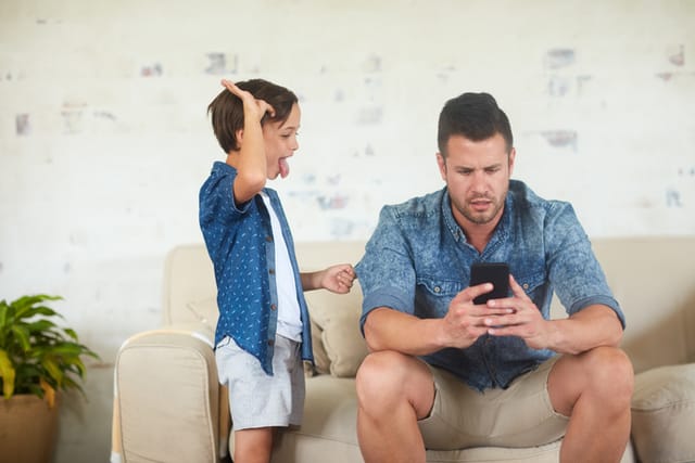 Shot of a man busy on his phone while his son is seeking for attention