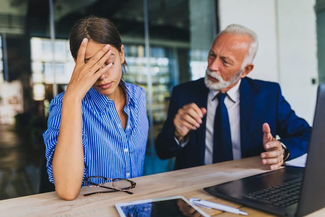 older businessman talking down to female employee