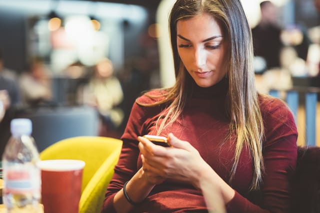 Young woman drinking coffee and using smartphone in the coffee shop
