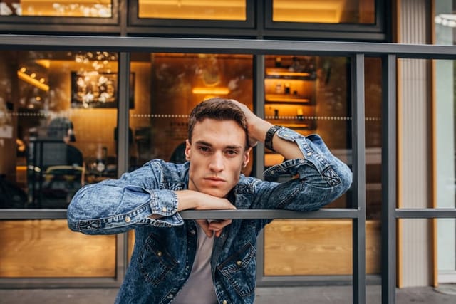 Handsome young man in denim shirt standing outdoors.